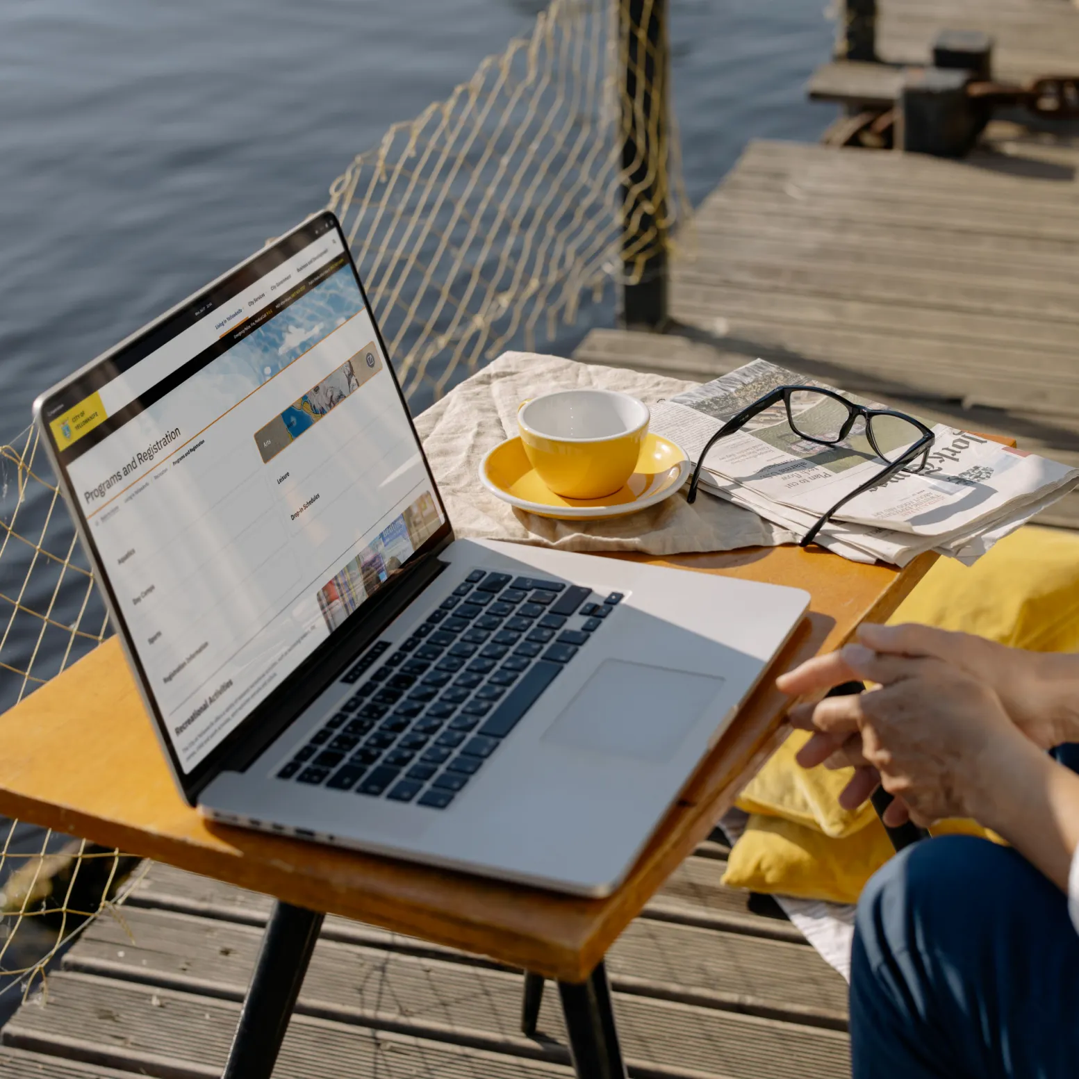 Person using a laptop displaying the City of Yellowknife programs and registration page at a lakeside dock