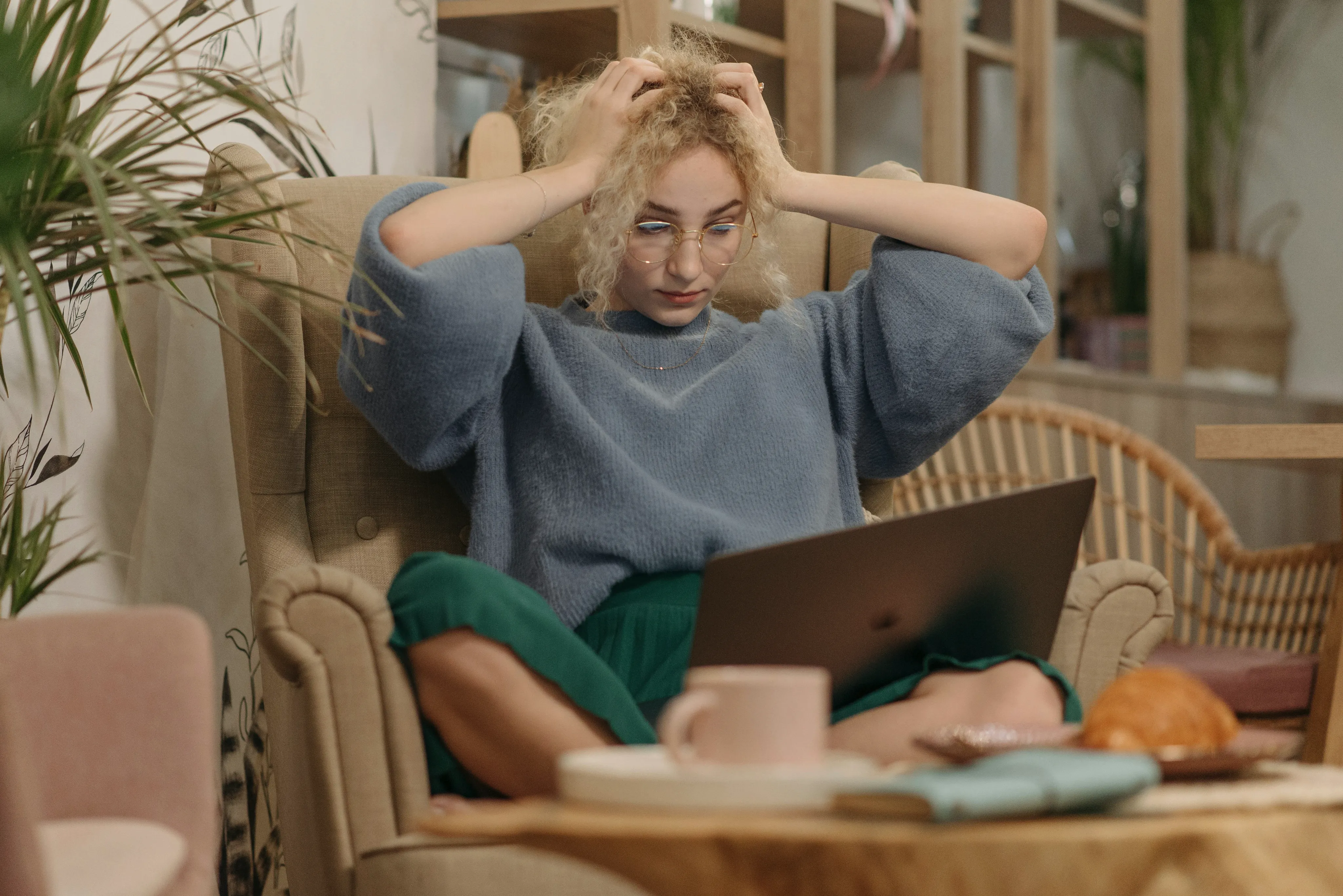 Person sitting in an armchair, holding their head while looking at a laptop