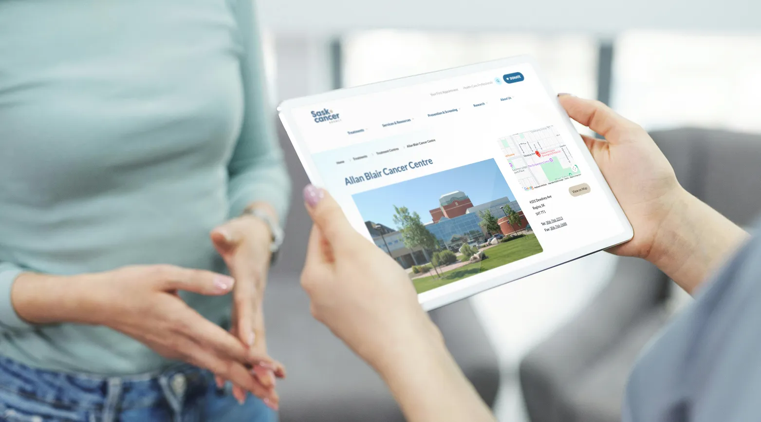 Two people reviewing the Sask Cancer Agency Allan Blair Cancer Centre page on a tablet